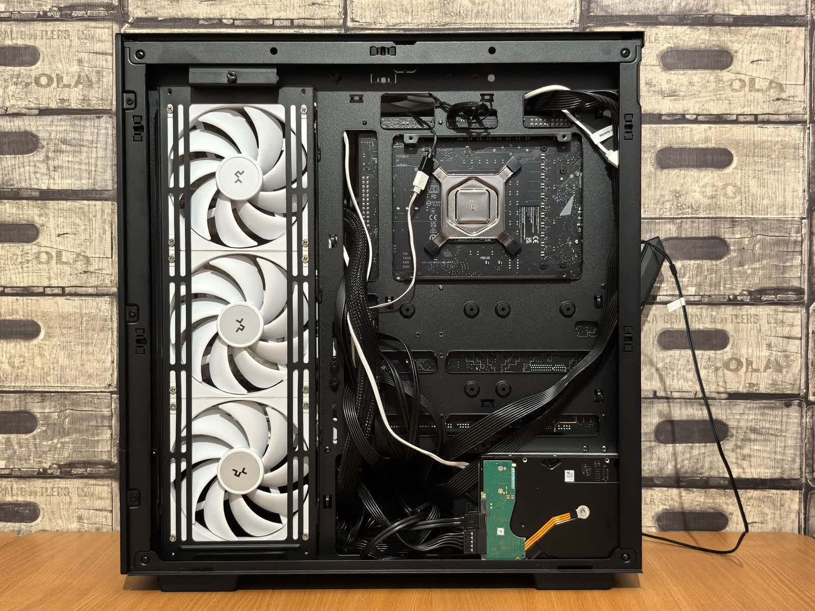 Gabinete de PC de escritorio abierto sobre un banco de trabajo, con la placa madre, los ventiladores y el disco a la vista.